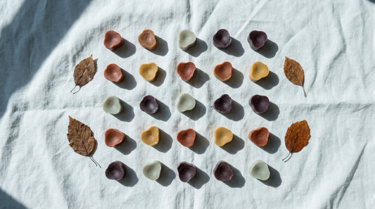 Best fall wax melt scents: wax melts in rust, ochre and deep plum arranged on bone-white linen with dry pressed leaves